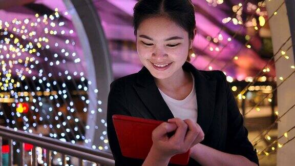 4K慢镜头:亚洲女商人在天桥上行走她在晚上玩平板电脑