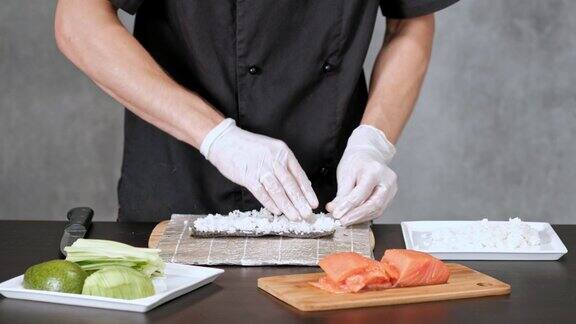 年轻的寿司厨师准备日本寿司卷米饭鲑鱼鳄梨和海苔餐厅厨房