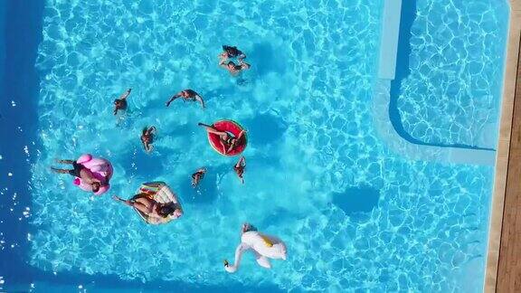 朋友们在游泳池里举行派对有充气的火烈鸟天鹅床垫在豪华度假村快乐的年轻人对着无人机摄像机挥手从以上观点穿着比基尼日光浴的女孩
