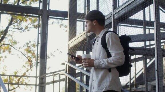 一个男人站在金属楼梯上一边用手机一边喝咖啡