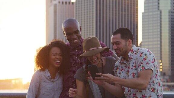 朋友们在手机上看日落时分曼哈顿的照片