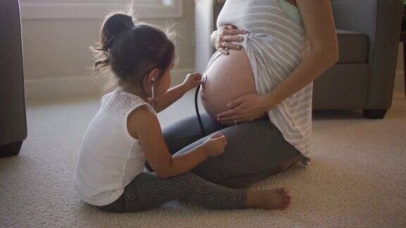 年轻的女孩听着她妈妈怀孕的肚子