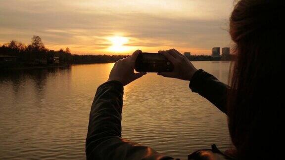 白种年轻女子在美丽的日落湖边拍照