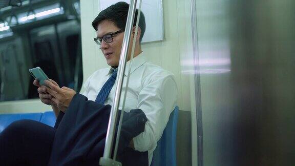 微笑的男性通勤者在地铁列车上用手机发短信