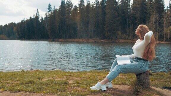年轻漂亮的金发美女坐在湖边的公园里看书侧视图