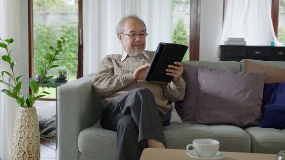亚洲退休老人用平板电脑在线转账或金融支付阅读文字微笑或大笑快乐和积极资深亚洲人具有数字技术理念