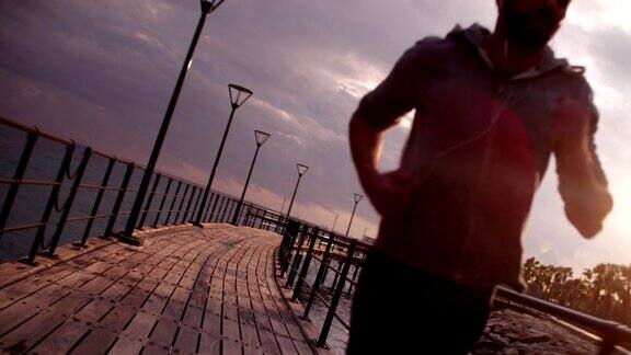 年轻的健康男子在日落边跑步边听音乐