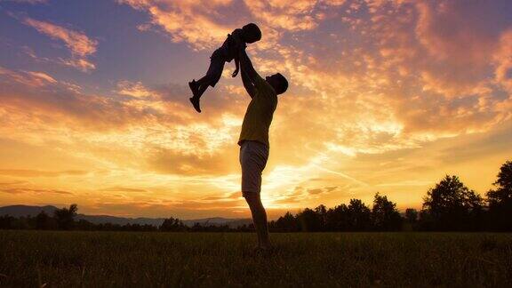 日落时分父亲将儿子抛向空中的剪影