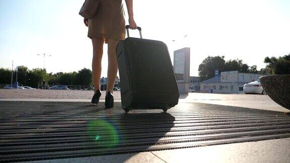 商务女士带着行李从机场去出租车停车场年轻女孩踩着高跟鞋用轮子滚动手提箱提着行李沿街走的女人旅行慢动作特写后视图
