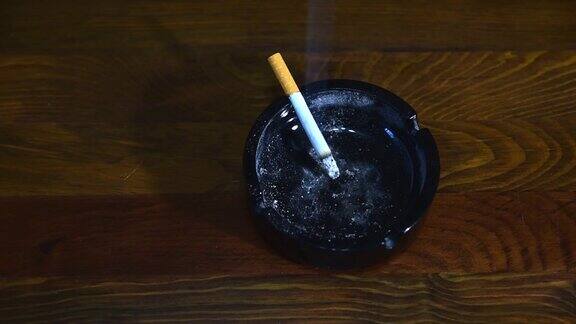 肮脏的黑色陶瓷烟灰缸和燃烧和吸烟的木制吧台桌上从上面看烟雾