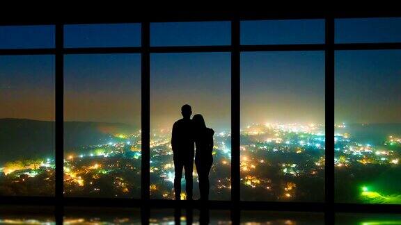 这对夫妻站在窗户旁以夜色中的城市为背景时间流逝