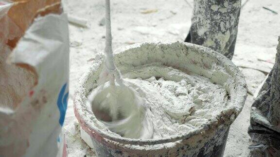 建筑工用电动搅拌机在桶中搅拌白色石膏