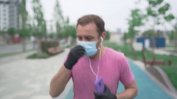 运动员戴着医用口罩和手套智能手机和耳塞在城市环境中慢跑