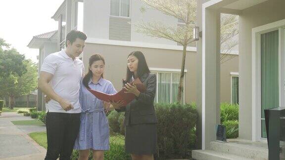 亚洲女人房地产经纪人展示了一个房子细节在她的档案以年轻的亚洲夫妇情人寻找和兴趣购买它买新房子