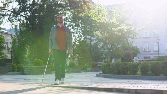 年轻盲人在户外独自行走时使用安全棍男性戴眼镜穿着休闲服独立