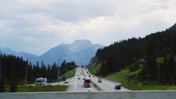 在加拿大阿尔伯塔省汽车沿着横跨加拿大的高速公路行驶背景是森林和加拿大落基山脉的阴天