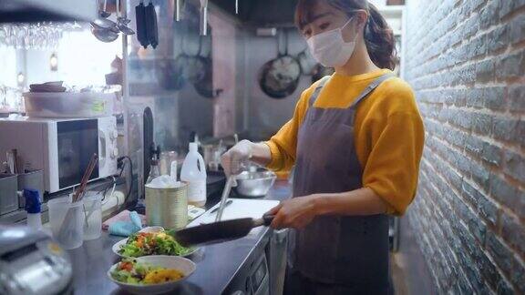 带防护口罩的女厨师在café和餐厅的商业厨房准备食物