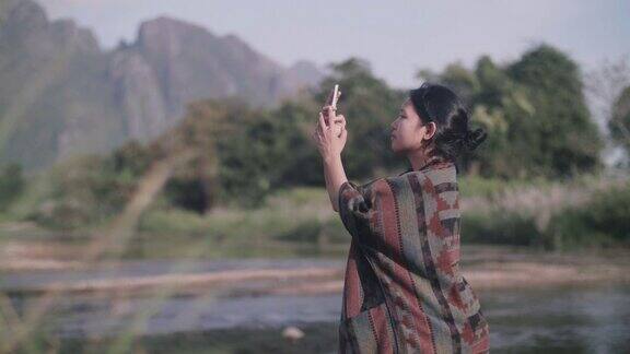 年轻女子站在河边用智能手机拍照