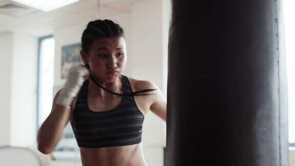年轻的亚洲女拳击手在她的拳击训练中双手包裹脸上紧张在室内健身房用巨大的力量打沙袋