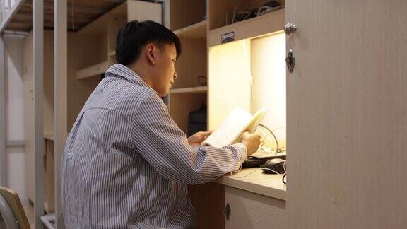 一个大学生正在宿舍里用手机放音乐看书