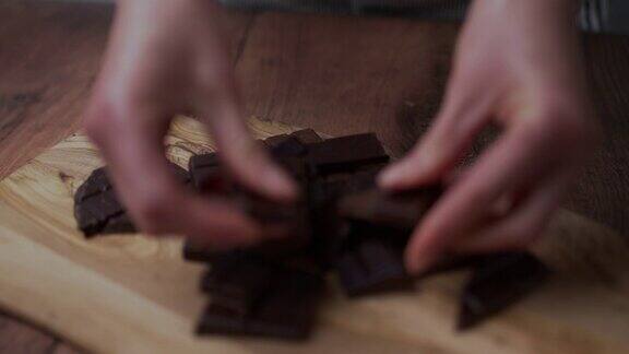 一个女人的手把一堆牛奶和黑巧克力撕成碎片放在一块木板和一张深色的木桌上