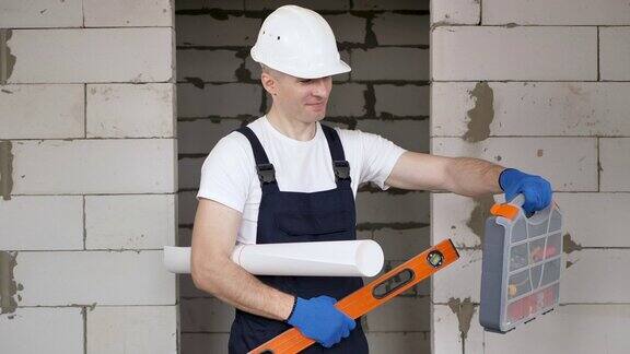 男性工人或建筑工人戴着头盔用水平仪、工具箱和蓝图靠砖墙