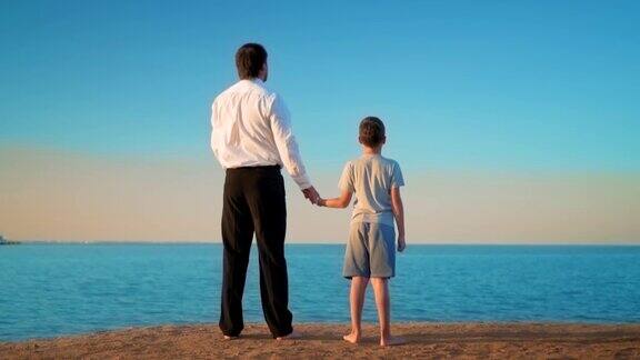 父子俩手挽着手站在海边父亲手指着远方