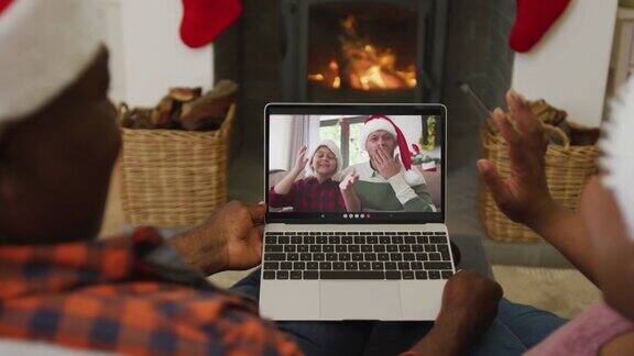一对戴着圣诞帽的非裔美国夫妇用笔记本电脑进行圣诞视频通话屏幕上是家人
