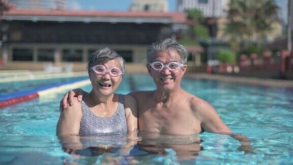 亚洲华人老夫妇看着镜头微笑在游泳池周末上午
