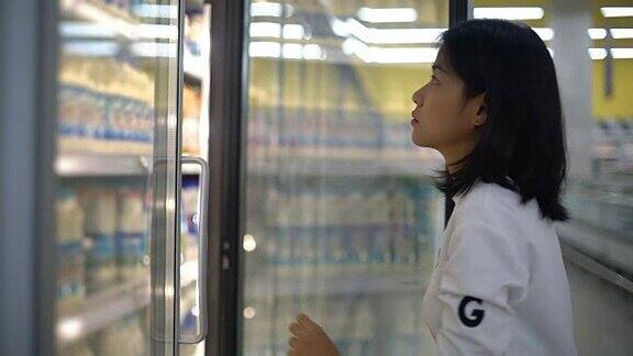 超市里从冰箱里拿出一瓶牛奶的女人