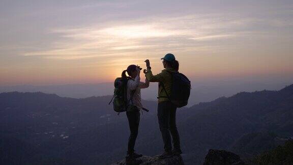 两个女人徒步上山在山顶上击掌举起双手庆祝成功