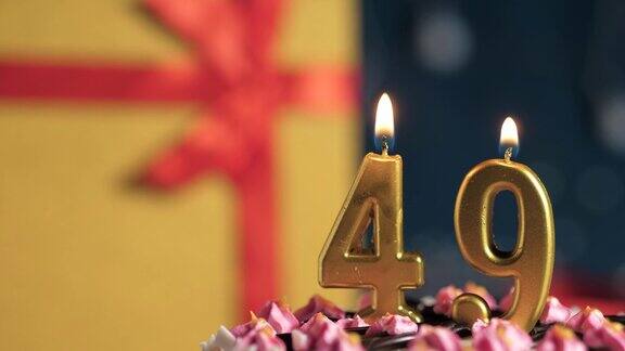 49号生日蛋糕用金色蜡烛点燃蓝色背景的礼物用黄色礼盒系上红丝带特写和慢动作