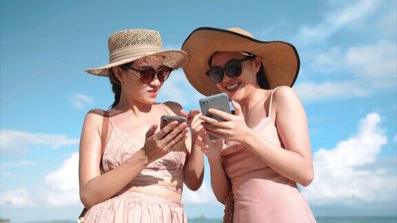 两个亚洲女人喜欢在海滩上一起使用智能手机