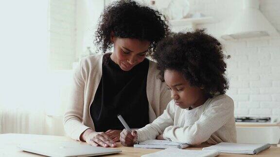 专注的小非洲裔美国女孩做作业和微笑的妈妈