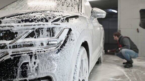 洗车时泡沫从一辆现代SUV上掉下来在汽车自动清洗站工人用刷子清洗汽车轮辋表面