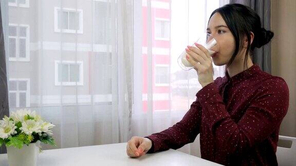一位年轻女子拿着一杯牛奶站在窗边