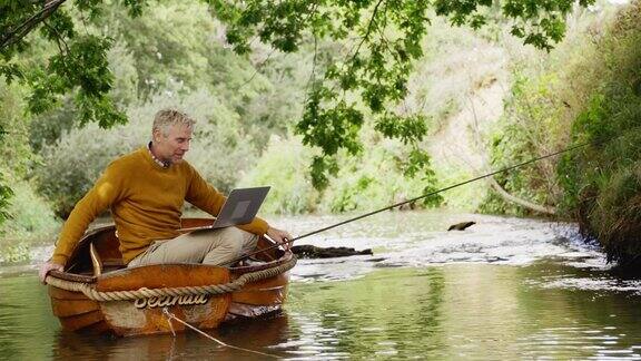 男子在河上的木船上飞钓和用笔记本电脑视频聊天