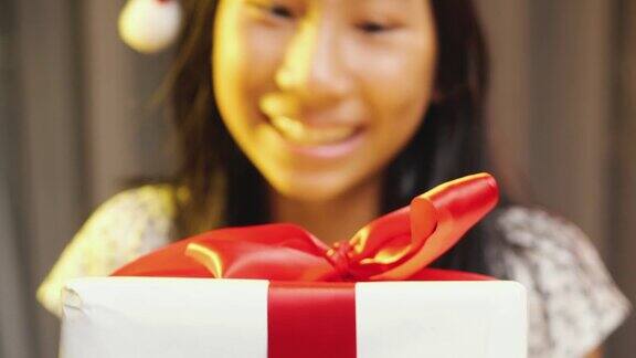 亚洲女孩戴着圣诞帽在家里拿着圣诞礼物的笑脸
