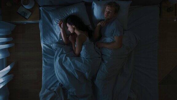夜景床:迷人的年轻夫妇睡在一起互相抱在怀里拥抱蓝色的夜间颜色和寒冷微弱的灯柱灯光透过窗户