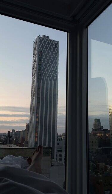 卧室里的女人透过全景窗户可以俯瞰曼哈顿的摩天大楼