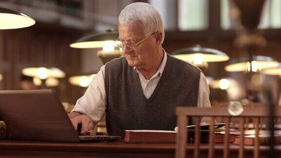 一位老人在图书馆里使用笔记本电脑和一本书