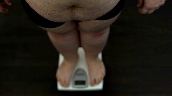 大肚子男人站在磅秤上检查体重节食结果