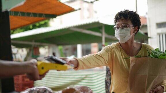 一名年轻女子在农贸市场用非接触式支付方式购买食品杂货戴着防护口罩