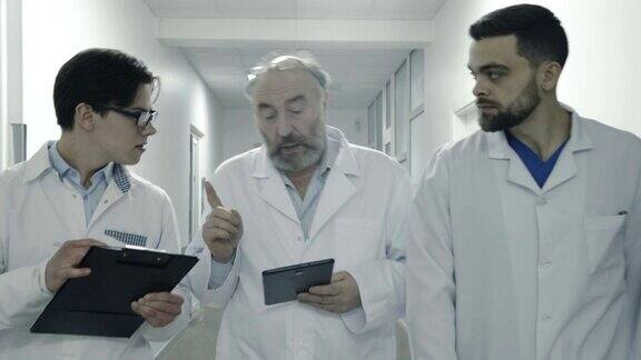 三名男医生走在医院走廊上讨论病人的笔记FullHD