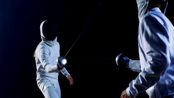 两名装备齐全的职业击剑手熟练地用剑剑格斗他们攻击防御跳跃刺和弓步拍摄孤立的黑色背景