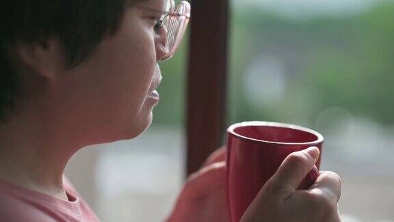 慢动作亚洲华人中年妇女享受她的热饮看着窗外放松的早晨