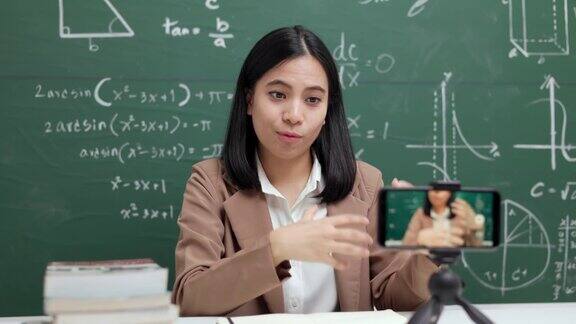 年轻的亚洲女教师坐在和学生视频会议女教师在课堂上通过智能手机在线课程直播培训数学