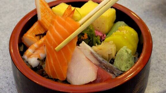 用筷子将新鲜生三文鱼和鸡蛋与芥末和蔬菜放入日式传统碗中在木桌上移动