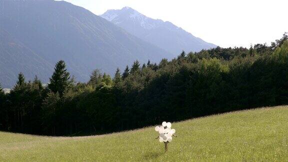 女孩拿着白色的气球在绿色的田野里散步