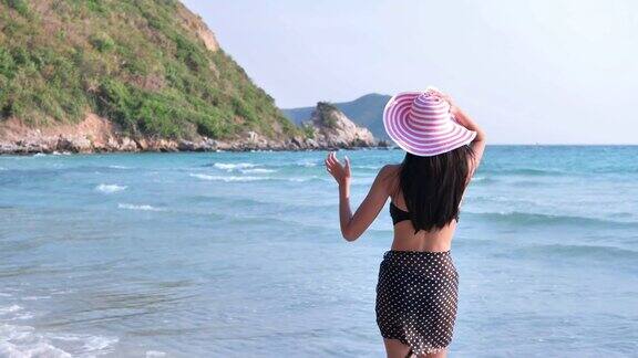 美丽的年轻亚洲女子在比基尼快乐享受散步和戴帽子在海上度假放松概念自由生活方式旅游度假慢动作